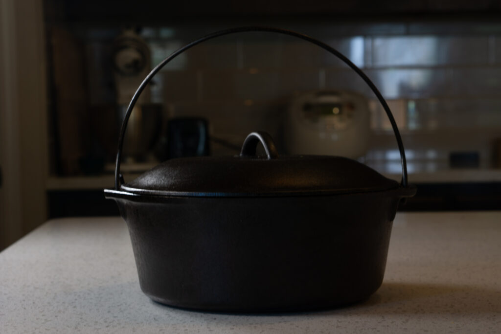 the fully restored Dutch oven with swing handle, deep dark matte seasoning, against the dark kitchen background